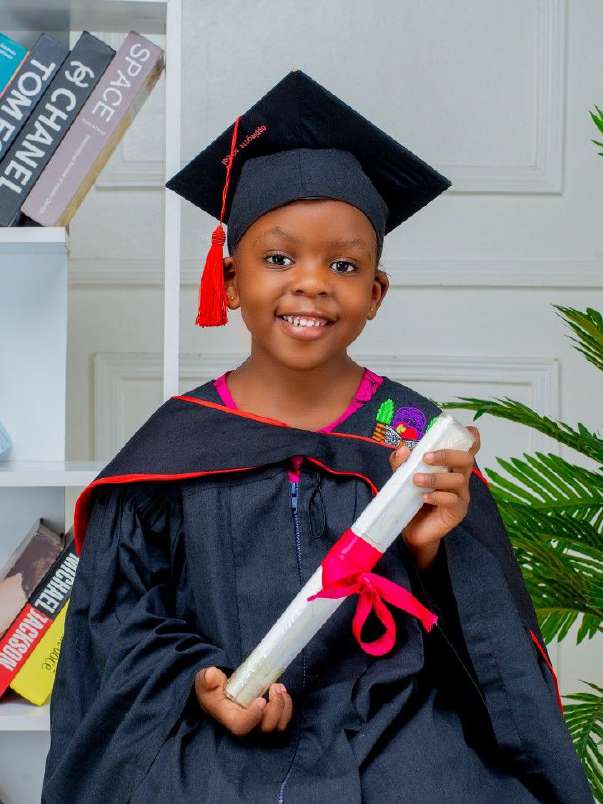 Young child in a graduation gown and cap holding a scroll