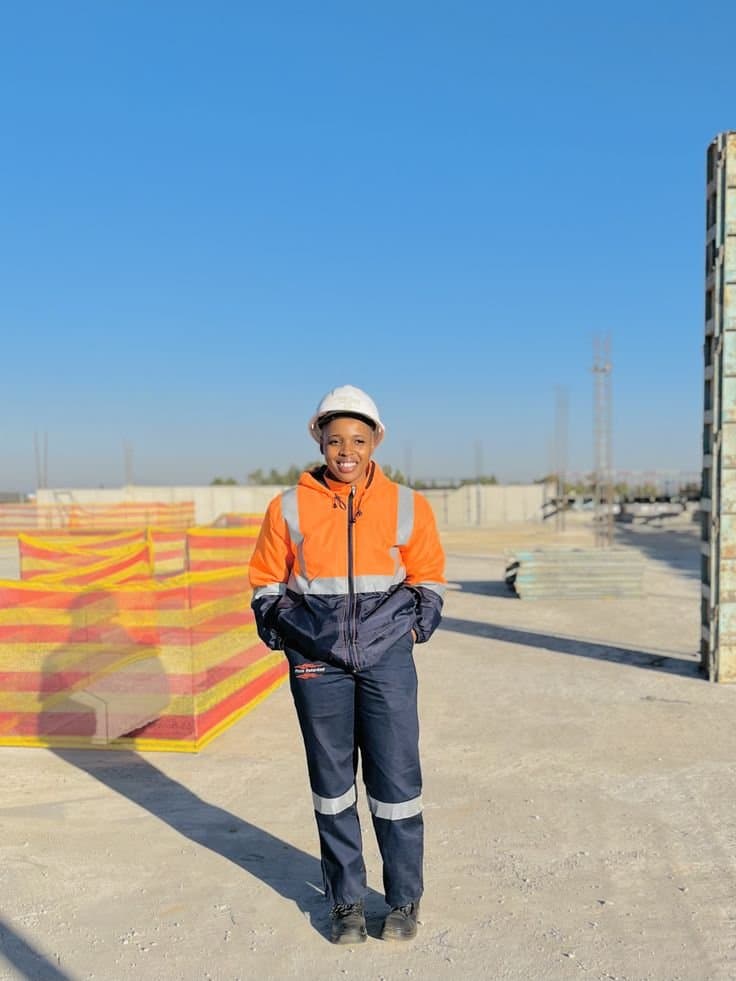 Smiling worker in a white hard hat, orange reflective jacket and navy work trousers on a building site