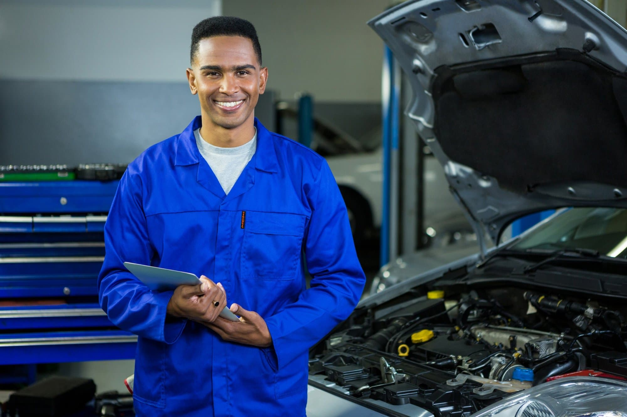Mechanic in a blue work jacket holding a tablet beside a car