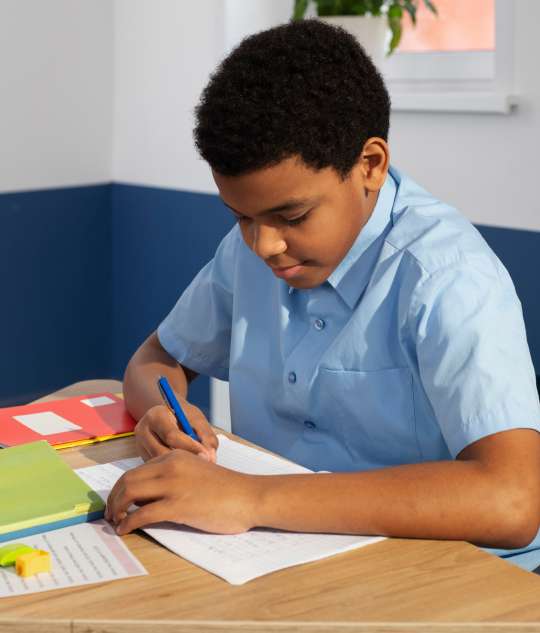 Pupil in a light blue school shirt writing at a desk